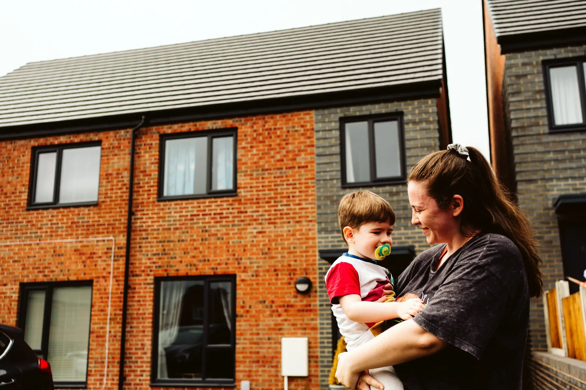 Woman holding a young child outside a terrace house.