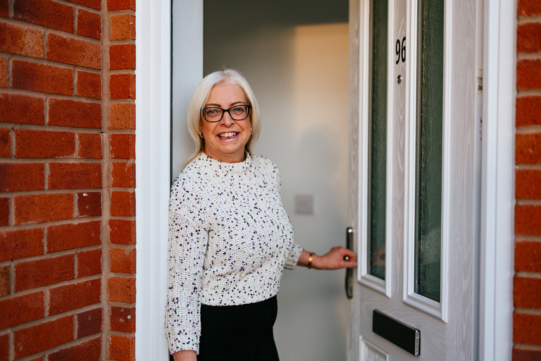 Lady stood at the front of her home, holding the handle for the front door.