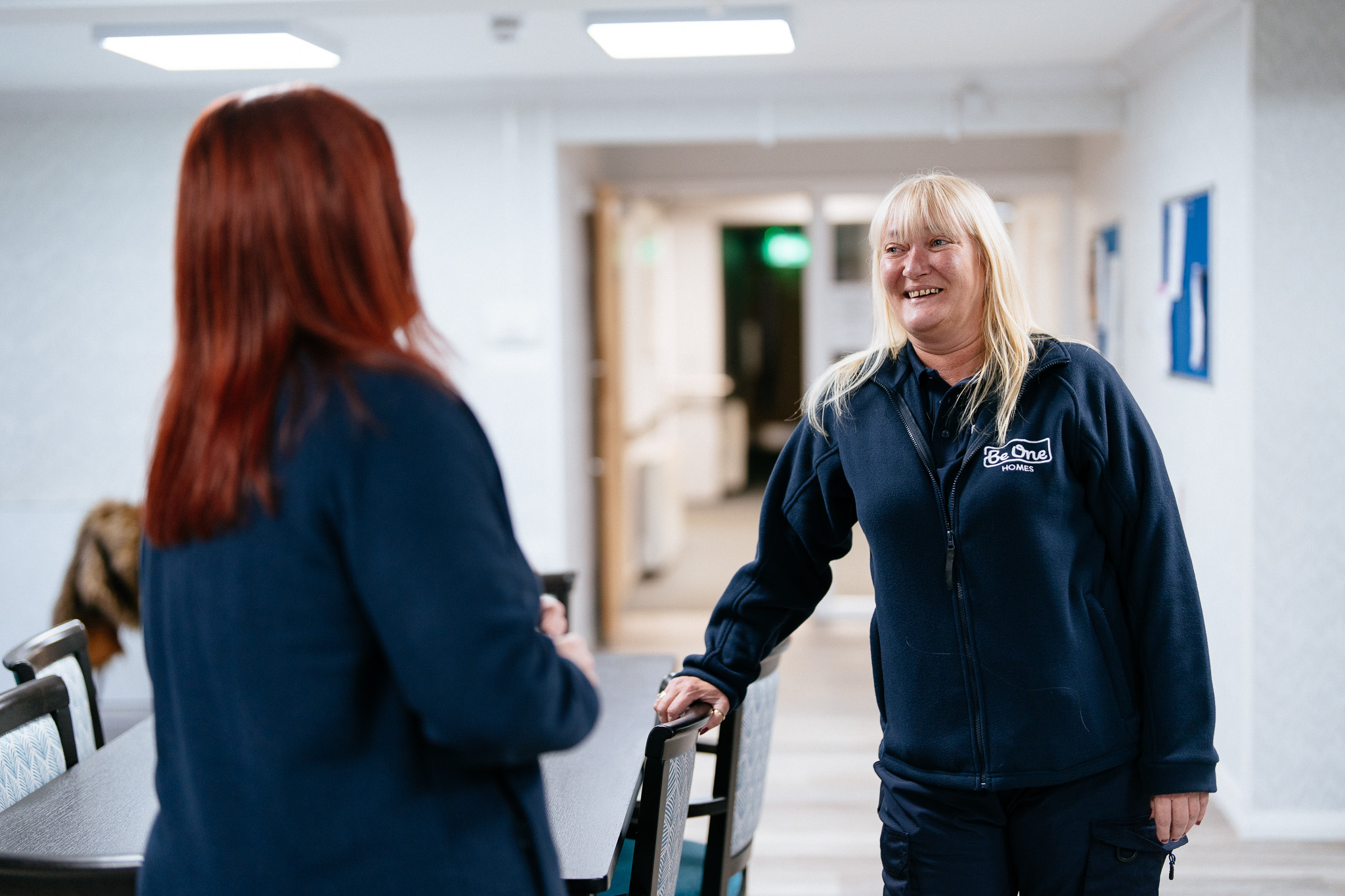 Two female Be One Homes colleagues talking to one another. They are wearing blue Be One Homes fleeces.