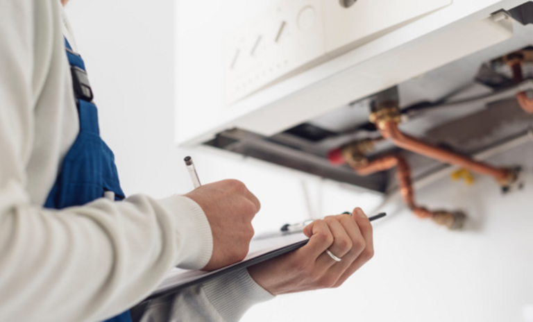 A Gas Engineer inspecting a boiler whilst holding a pen and clipboard.