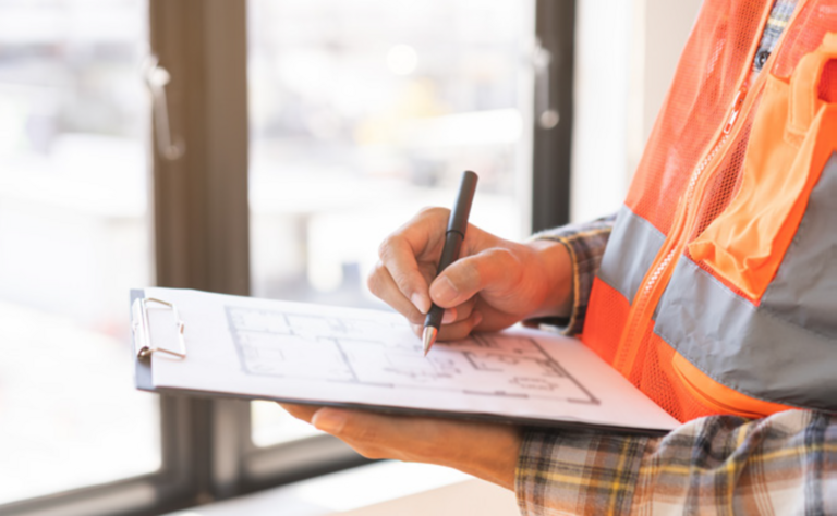 A person wearing a high visibility jacket whilst writing notes onto paper attached to a clipboard.