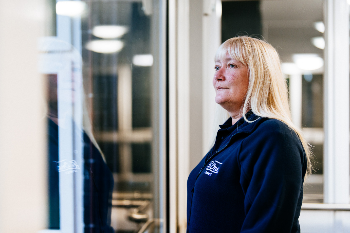 A female Be One Homes colleague stood looking out of a window. She is wearing a blue Be One Homes fleece.