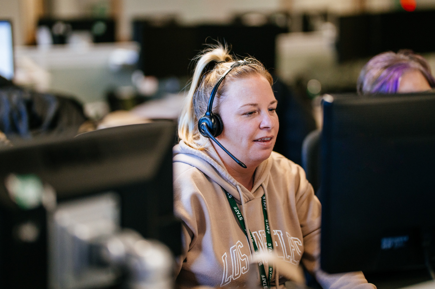 A female Be One Homes colleague sat using a computer. She is wearing a headset.