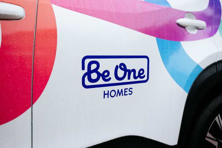 The Be One Homes logo and multicoloured brand threads on the side of a Careline vehicle.