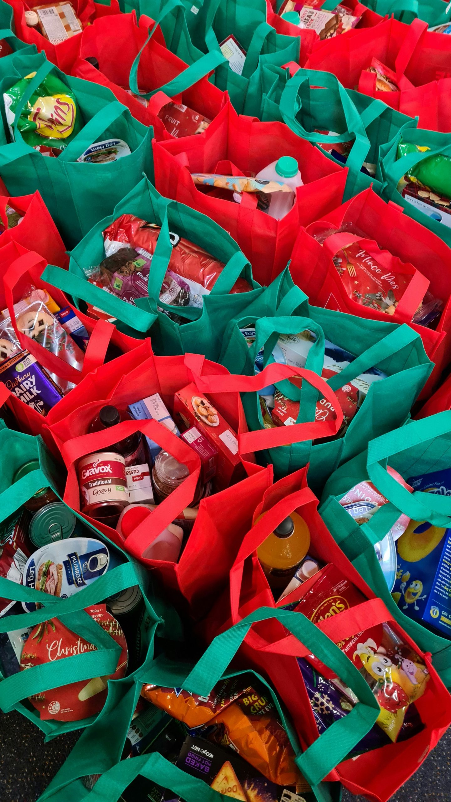 Bags of food shopping lined up next to one another. The bags are made from a fabric material and are either green or red in colour.