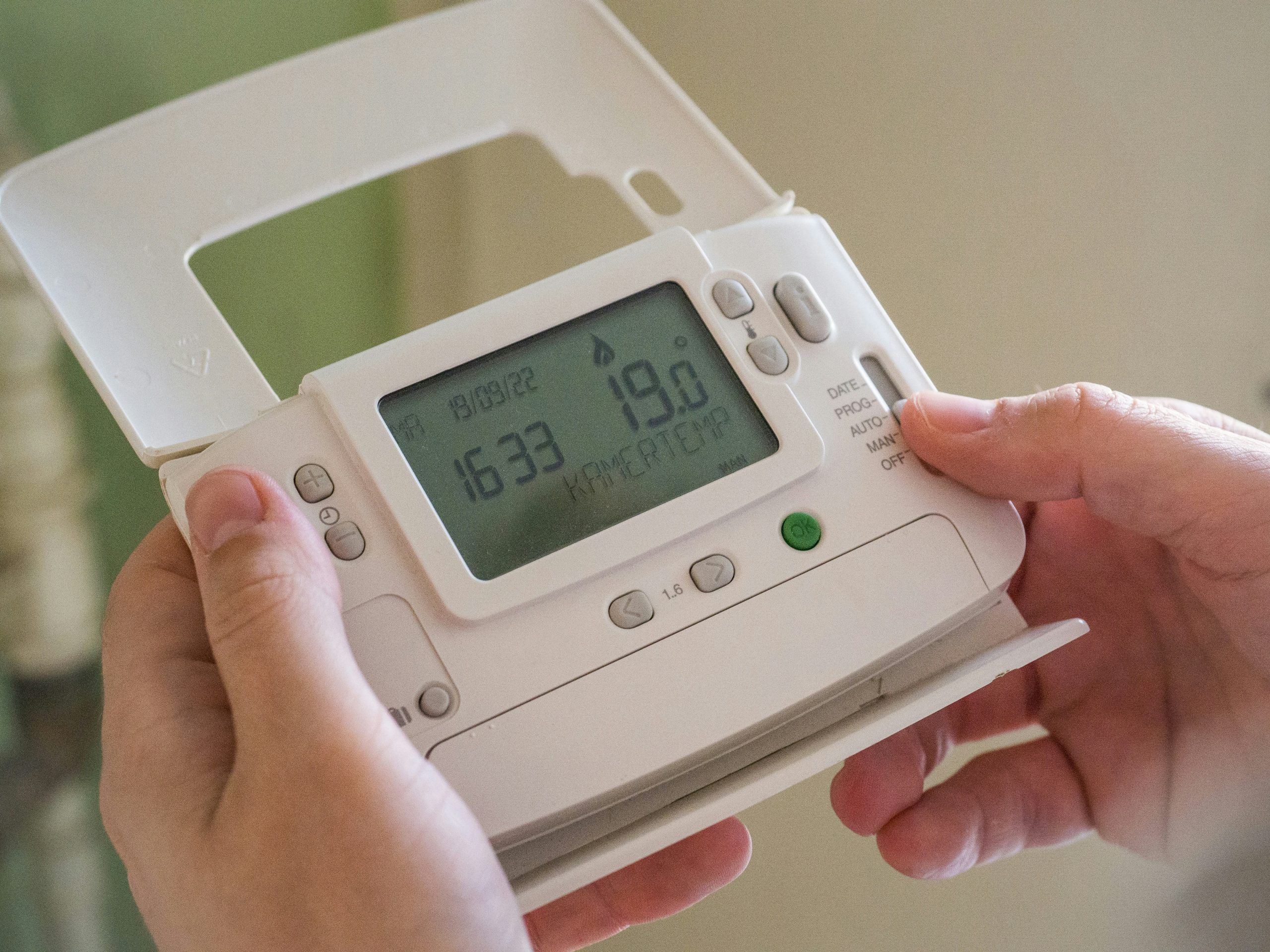 A wireless control unit for a central heating system. Someone is holding the unit as they adjust the temperature.