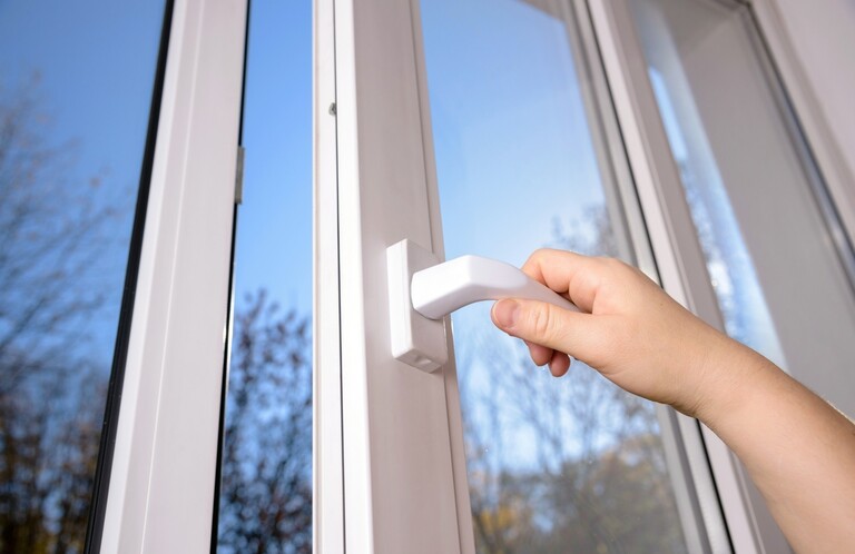 A low angled shot of a double-glazed window. Someone is opening the window using the handle.
