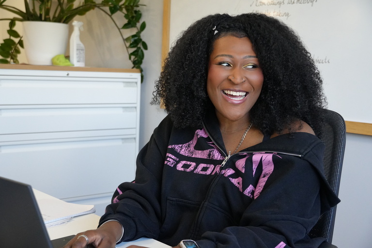 A Be One Homes colleague sat at her desk. She is looking to her right as she smiles at another colleague who isn't visible in the photo.
