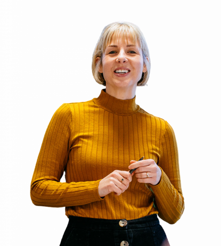 A female Be One Homes colleague. She is stood up, holding a pen, and is smiling towards the camera.