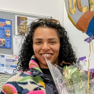 Portrait image of Ebony, who completed her university placement at our Bolton UCAN Centre. She is smiling whilst holding a bunch of flowers and a balloon.