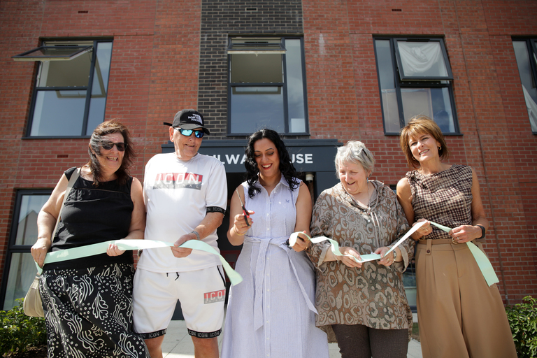 Kirith Entwistle MP cuts the ribbon at the opening of a newly developed apartment building, joined by Noel Sharpe, Chief Executive of Be One Homes, Sasha Deepwell, Chief Executive of Irwell Valley Homes, and other attendees.
